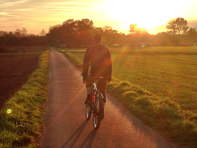 Eine Person fährt mit dem Fahrrad auf einem Weg bei Sonnenuntergang.