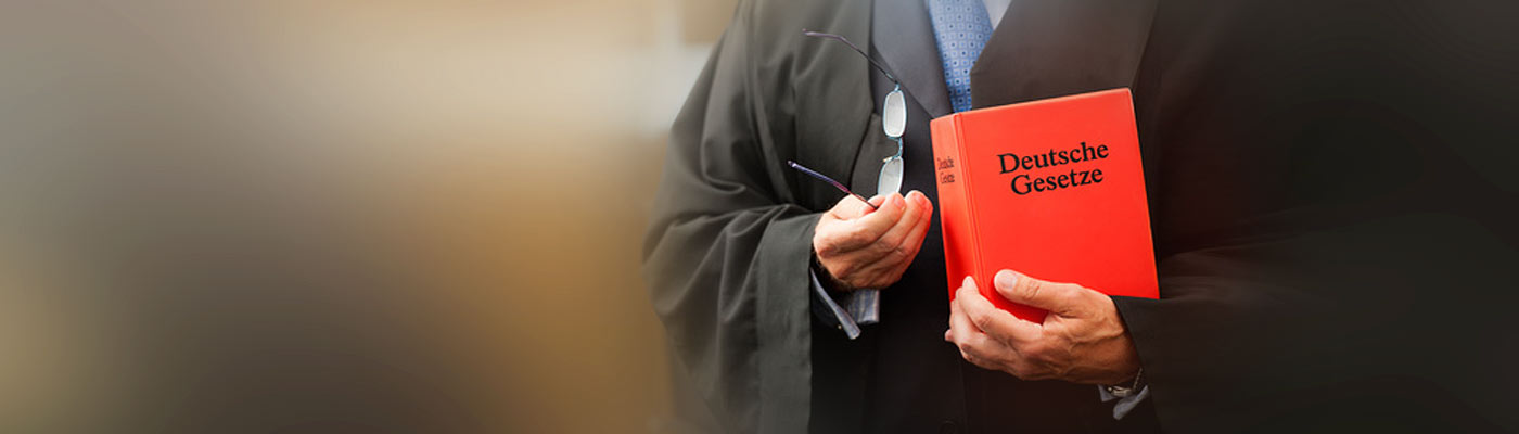 Ein Richter hält ein rotes Buch mit dem Titel "Deutsche Gesetze".